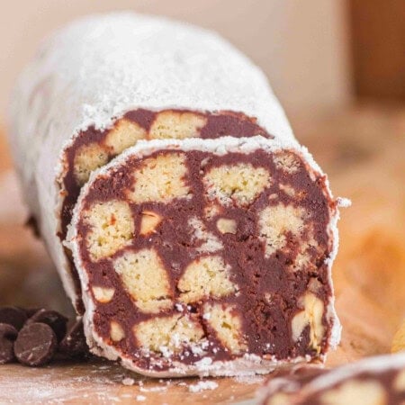 A sliced chocolate biscuit salami dusted with powdered sugar on a wooden surface.