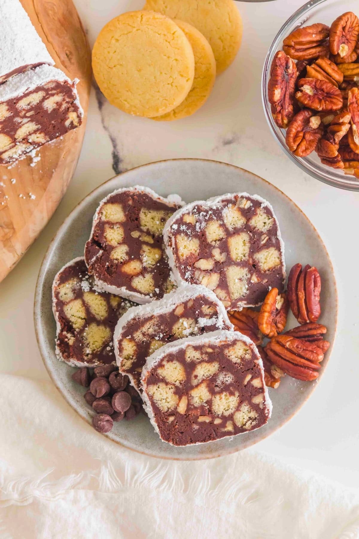 Plate with chocolate biscuit slices, pecans, chocolate chips, and cookies nearby.