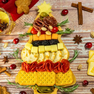 Festive Christmas tree-shaped charcuterie board with cheese, crackers, and meats.