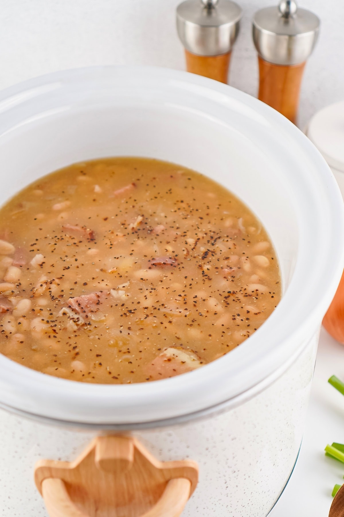 A slow cooker filled with bean soup, topped with black pepper.