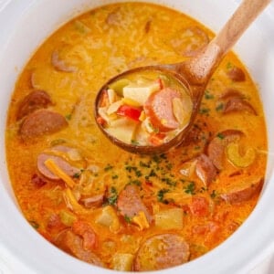 Creamy sausage and potato soup in a pot with a wooden ladle.