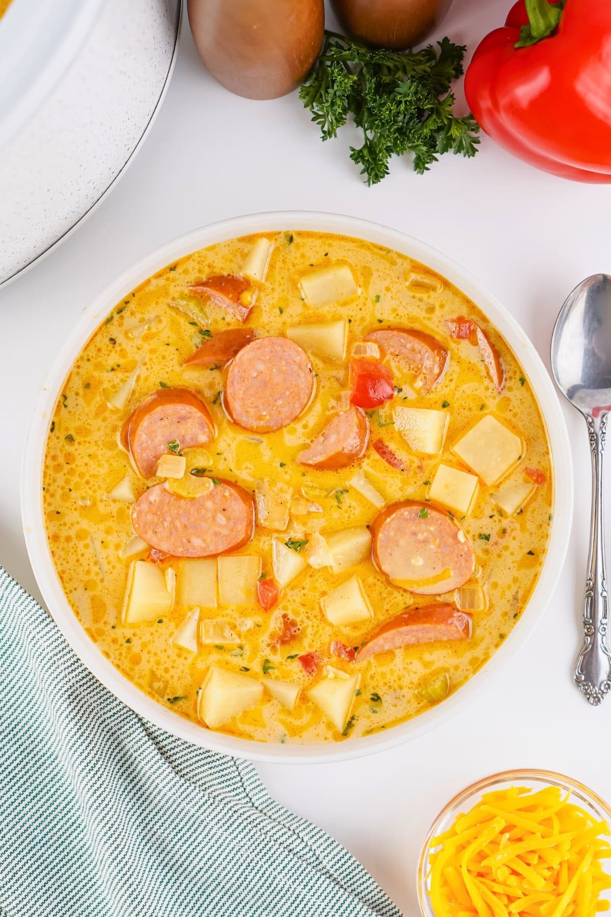 Bowl of creamy sausage and potato soup with diced vegetables on a white table.