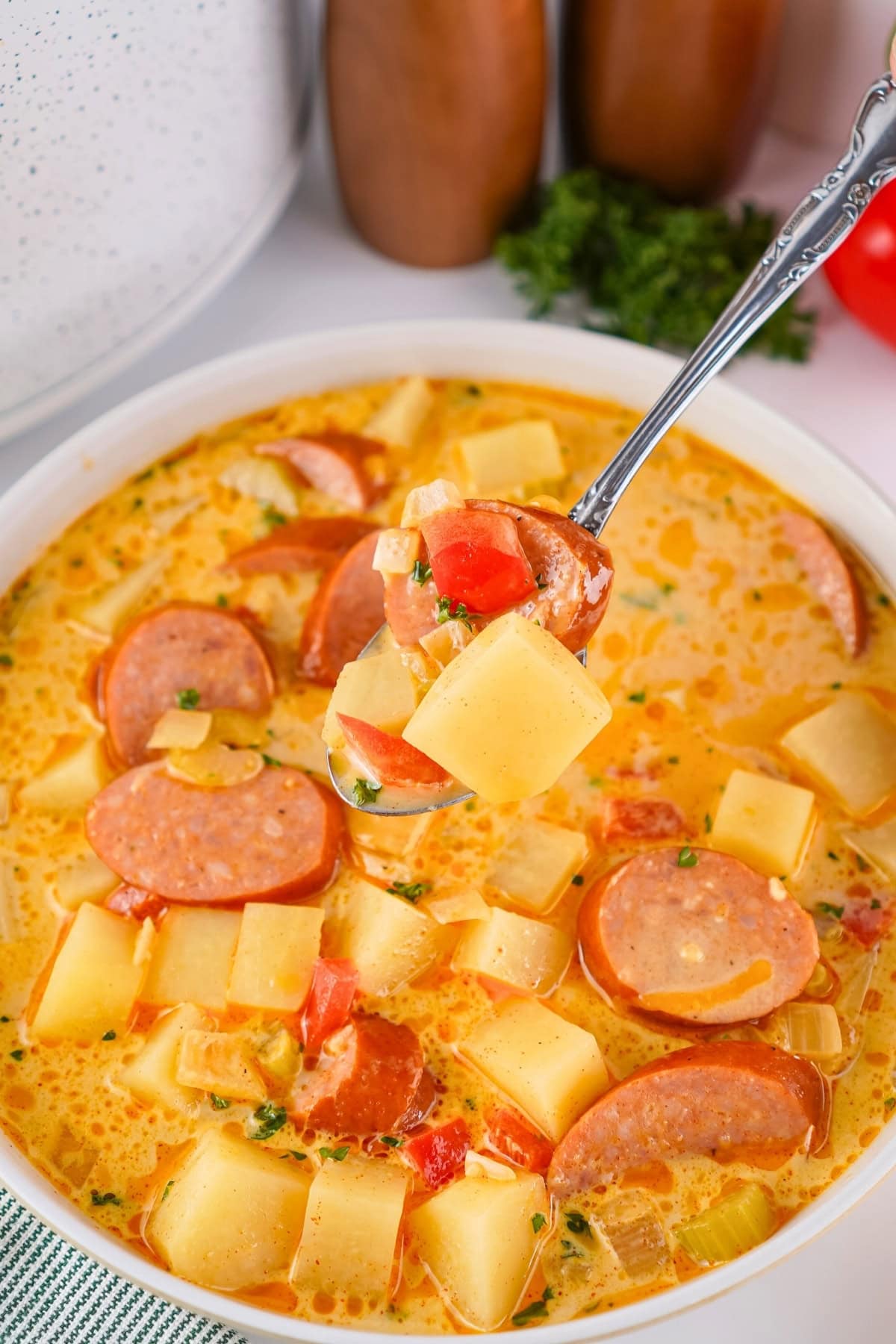 A spoonful of creamy sausage and potato soup with tomatoes and herbs.