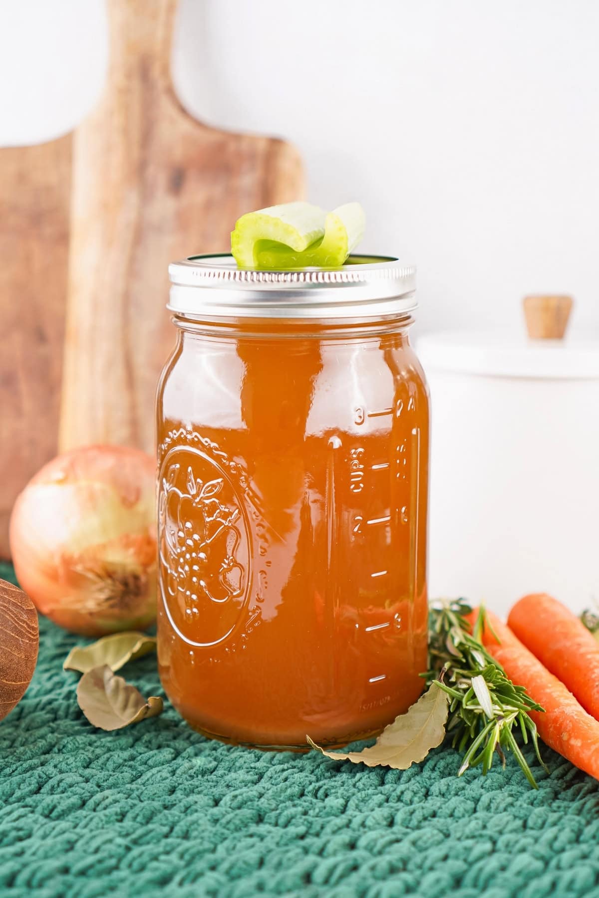 A jar of vegetable broth sits on a green mat with fresh vegetables around it.