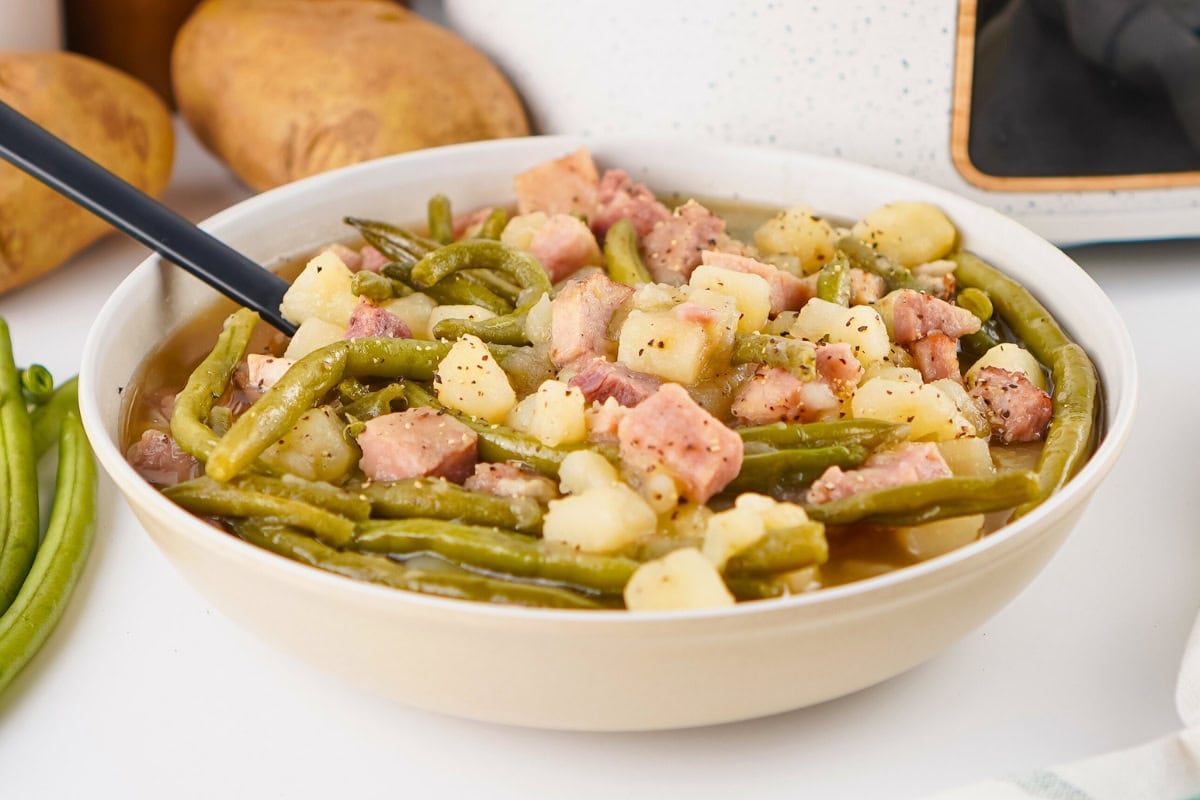 Bowl of green beans, potatoes, and ham with a spoon.