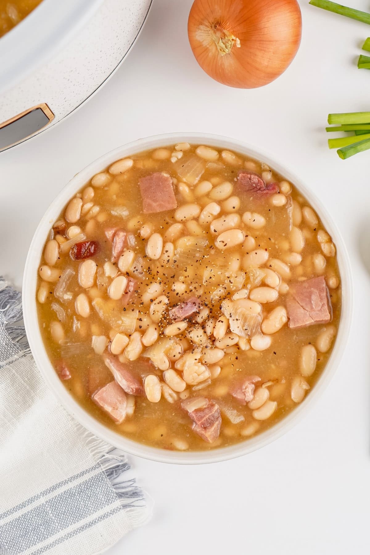 A bowl of ham and bean soup garnished with black pepper on a white table.
