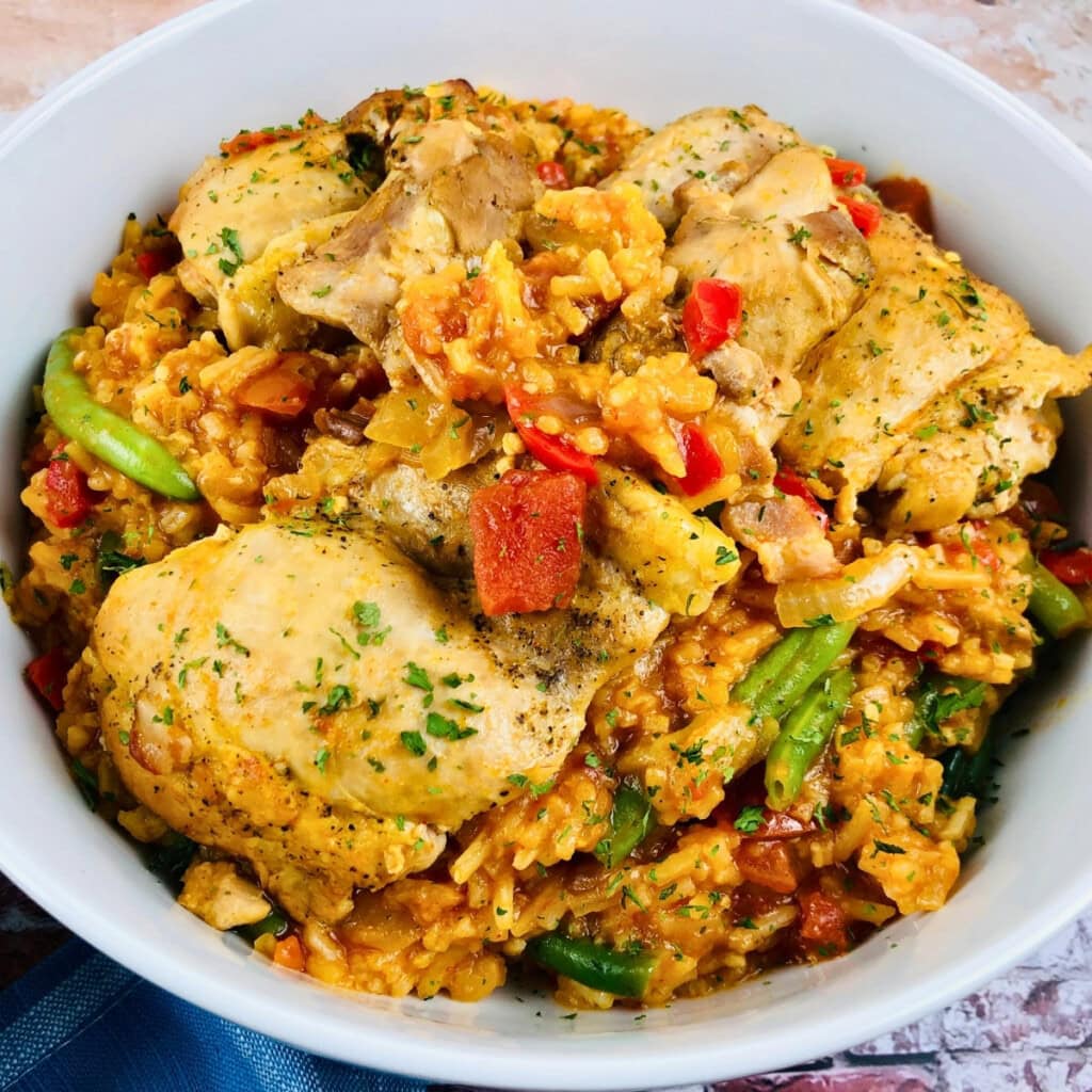 A bowl of seasoned chicken with rice, green beans, and diced red peppers.