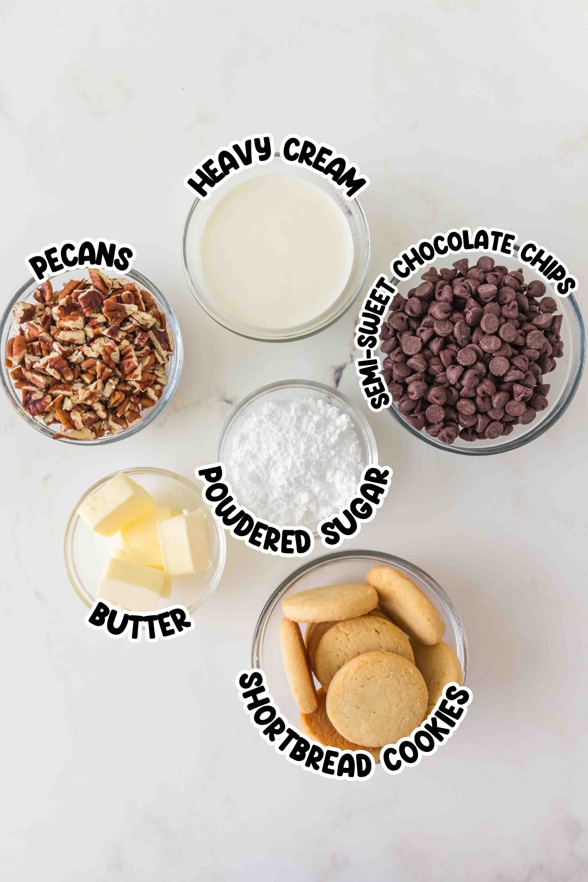Five bowls with heavy cream, pecans, semi-sweet chocolate chips, butter, and cookies.