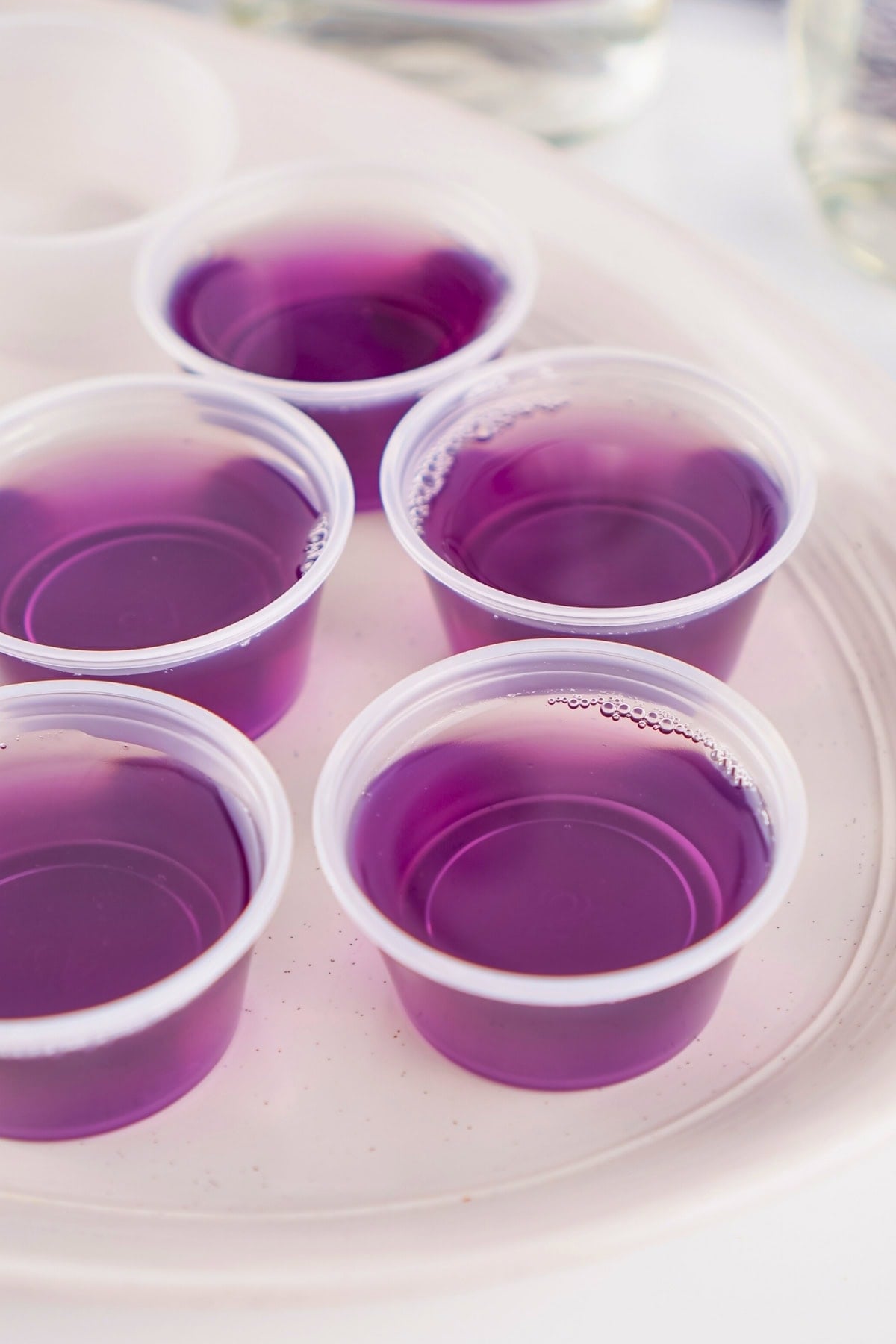 Five small plastic cups filled with purple liquid on a white tray.