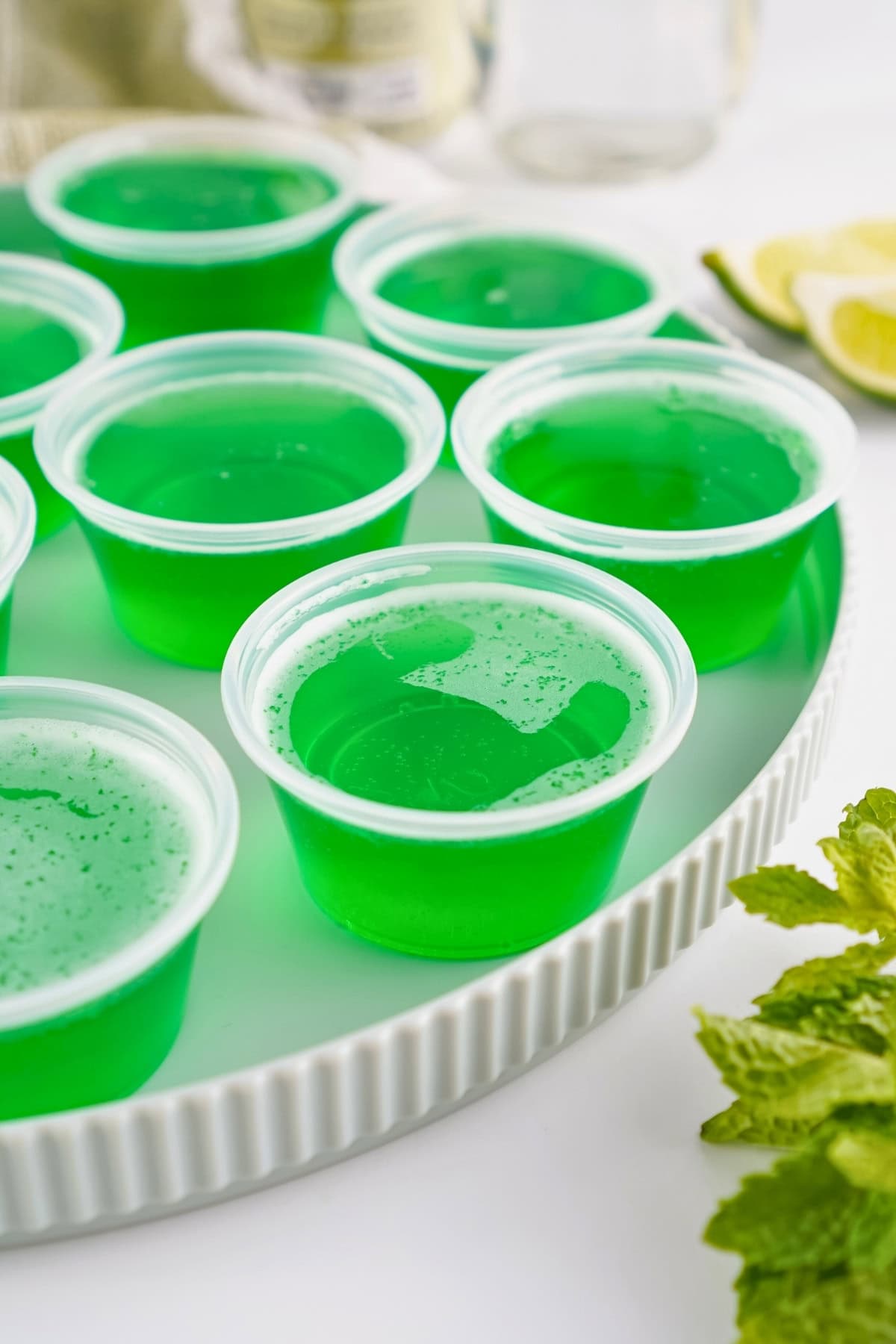 Green gelatin shots in small plastic cups arranged on a white tray.