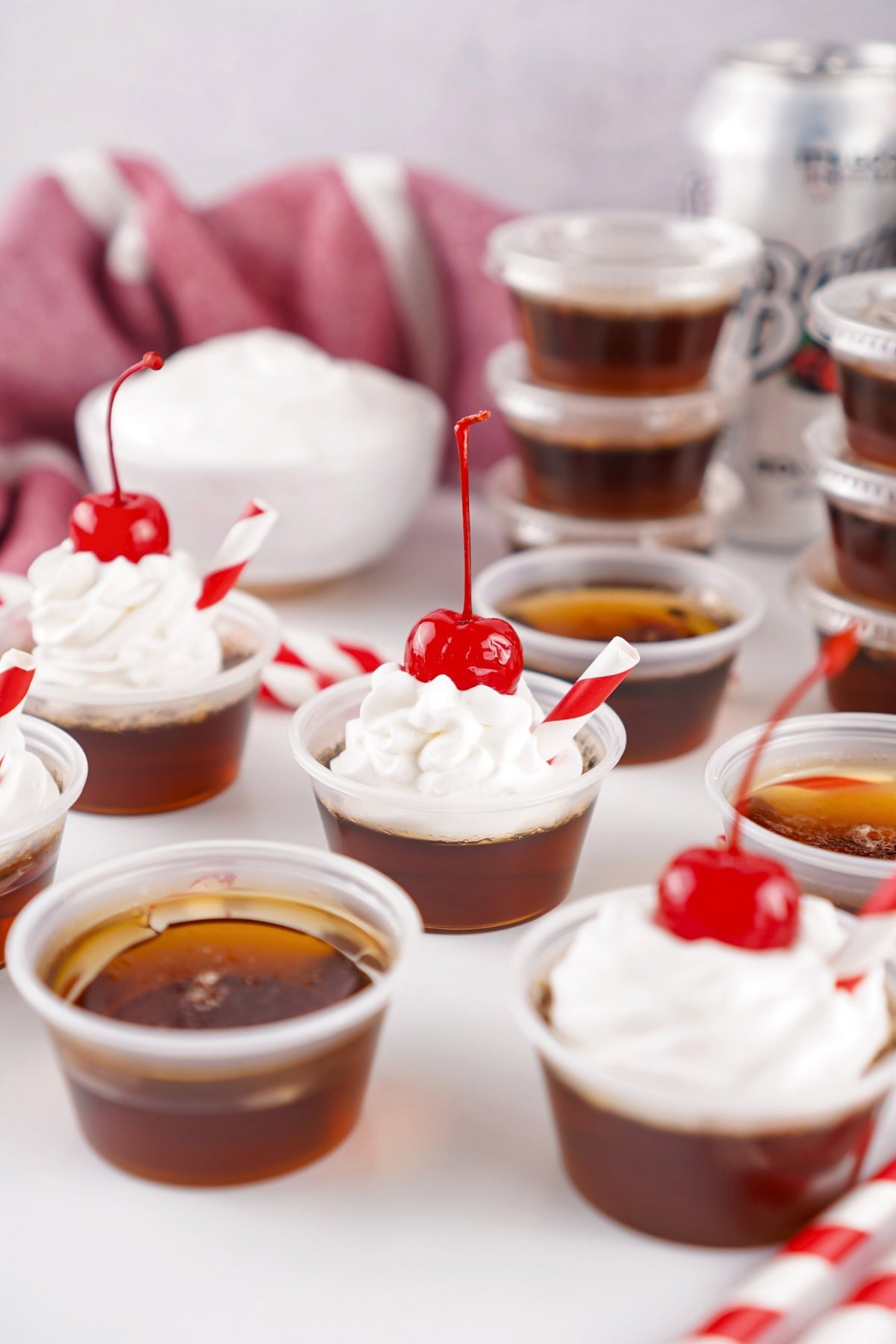 Mini root beer float shots topped with whipped cream and cherries, with straws.