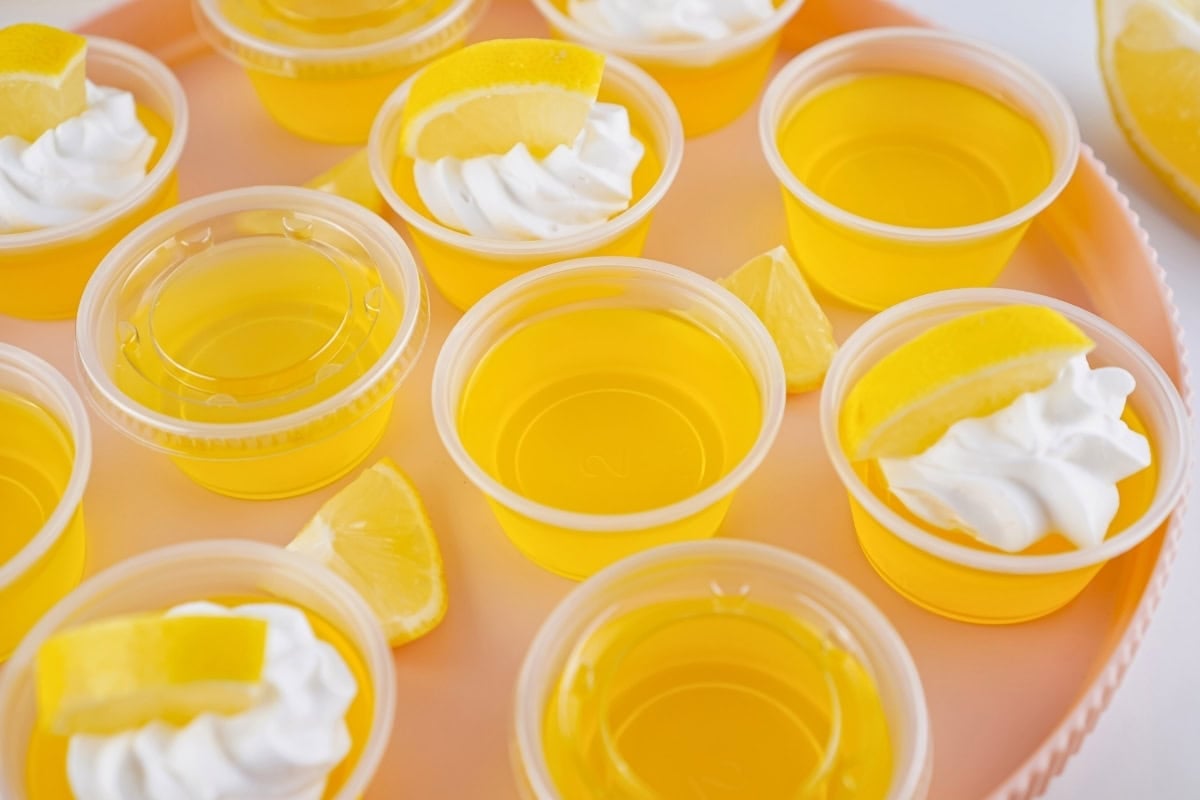 Yellow gelatin cups with whipped cream and lemon wedges on a peach tray.