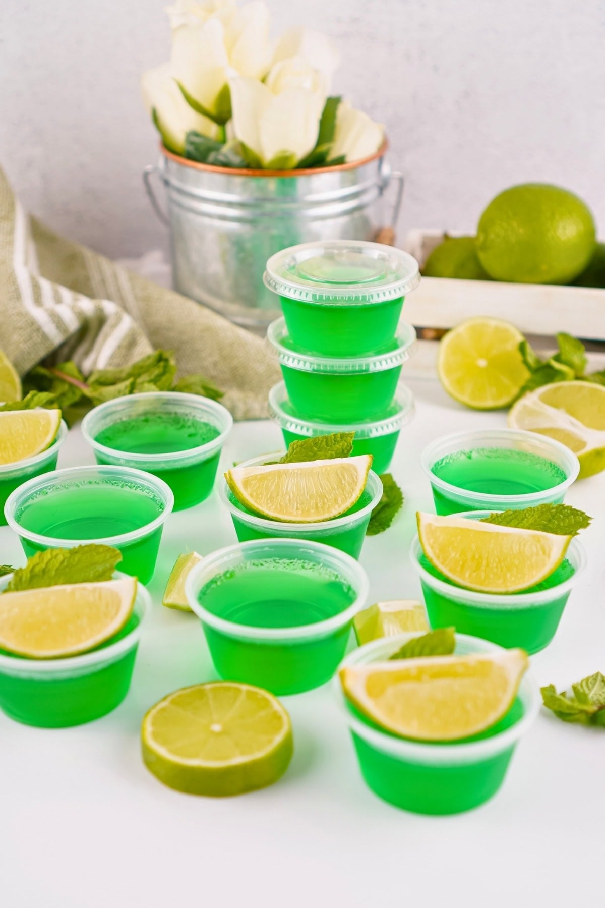 Green gelatin shots in plastic cups, garnished with lime wedges and mint leaves.