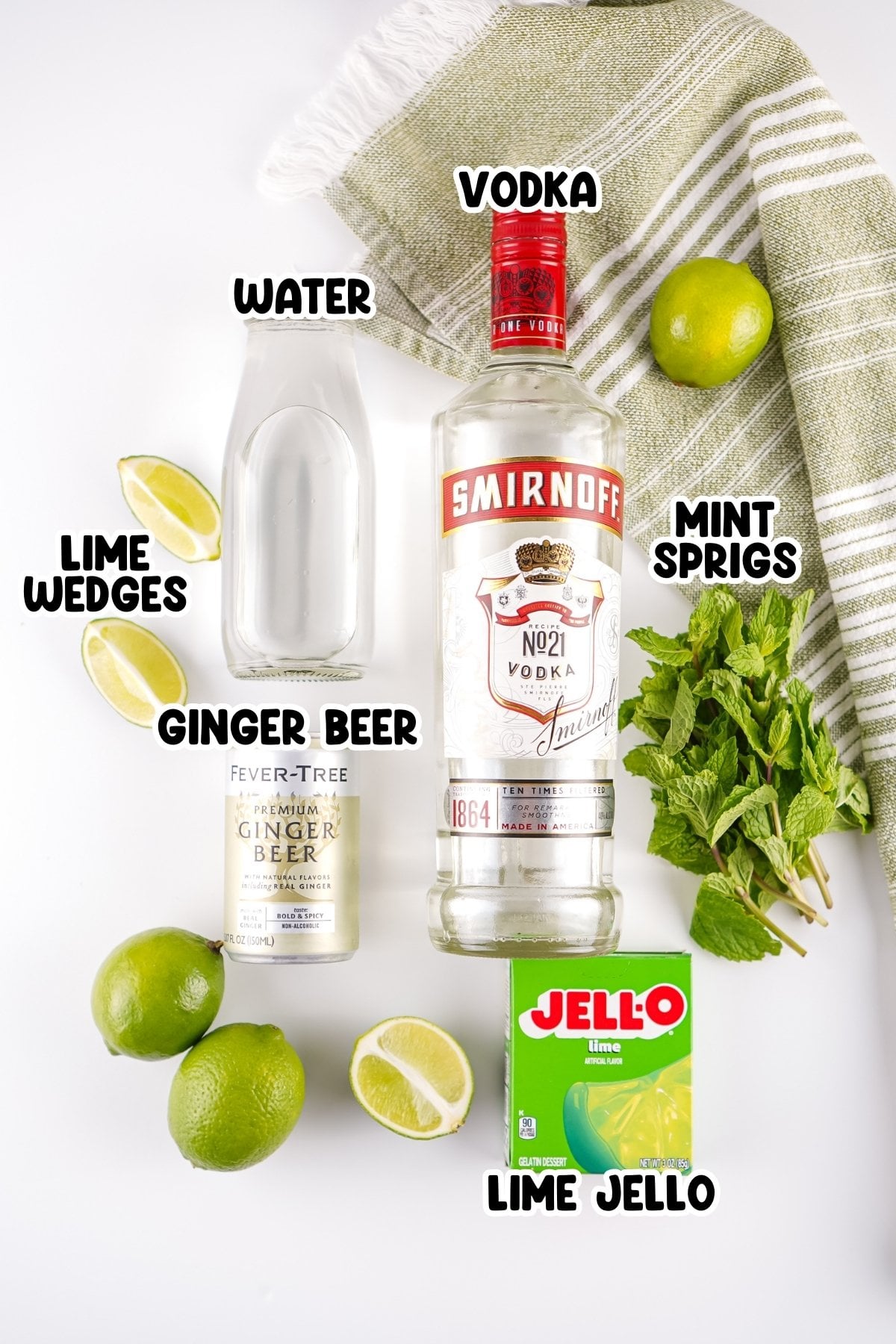 Vodka, ginger beer, lime jello, water, limes, and mint sprigs on a white surface.