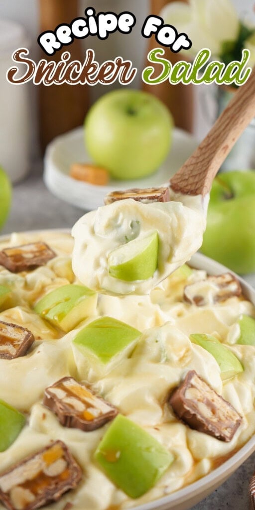 A spoon scoops Snickers salad with apple chunks and candy bars from a bowl.