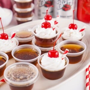 Mini root beer float jello shots topped with whipped cream and cherries.