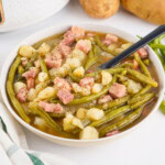 A bowl of green beans, potatoes, and ham stew with a black spoon.