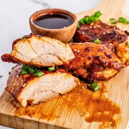 Sliced grilled chicken breast with sauce and green onions on a wooden board.