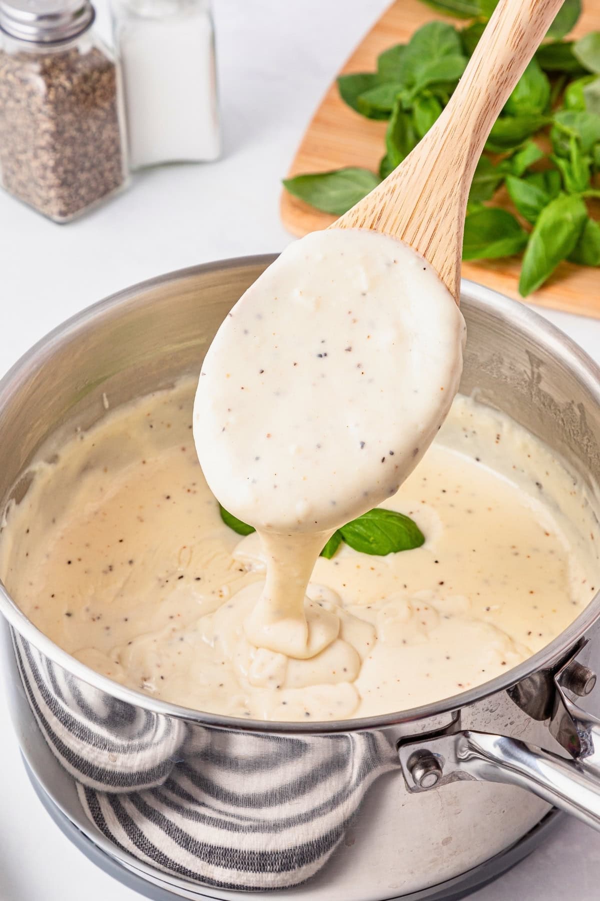 Creamy white sauce being stirred in a pot with a wooden spoon.