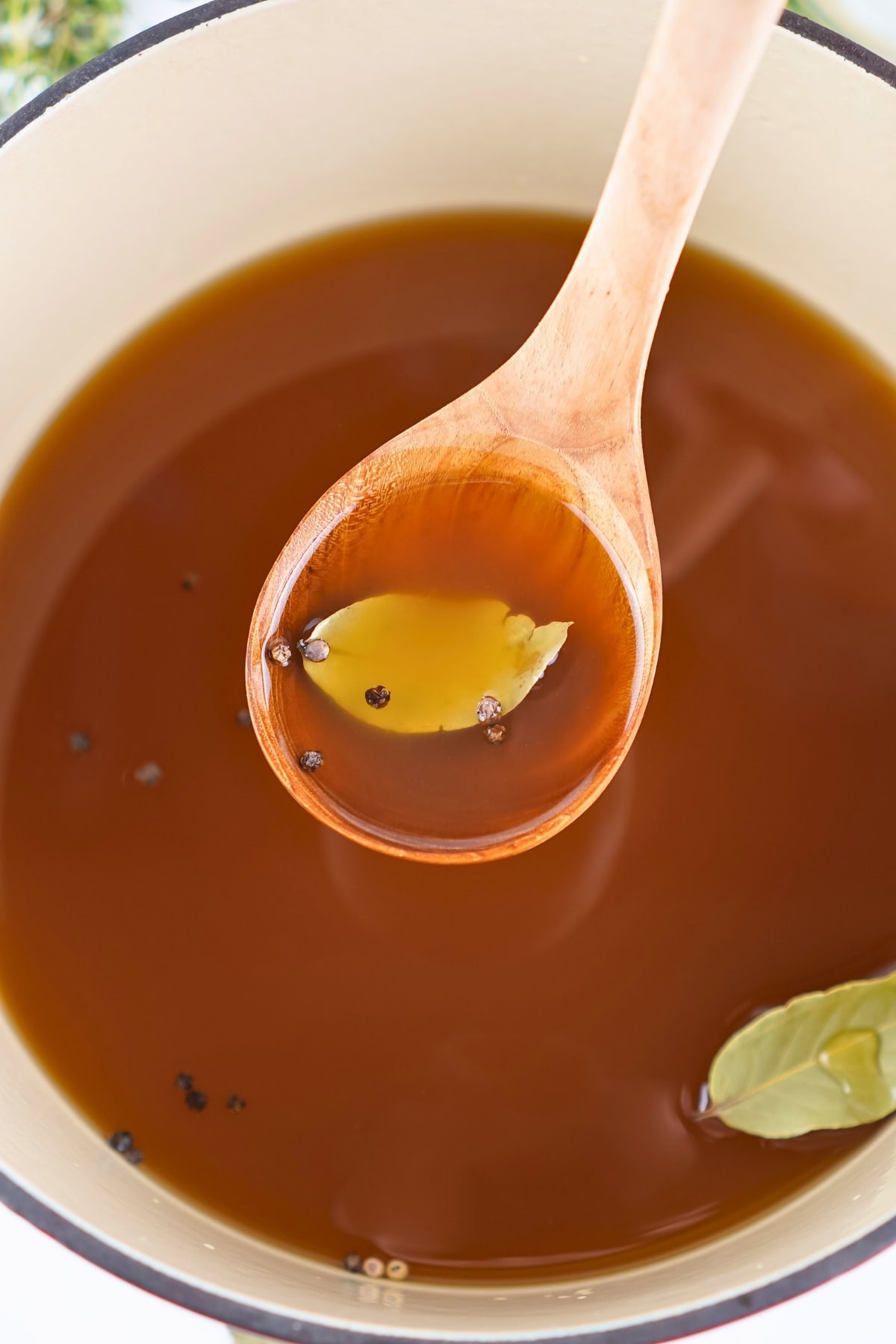 Wooden spoon with broth, a bay leaf, and peppercorns in a pot.
