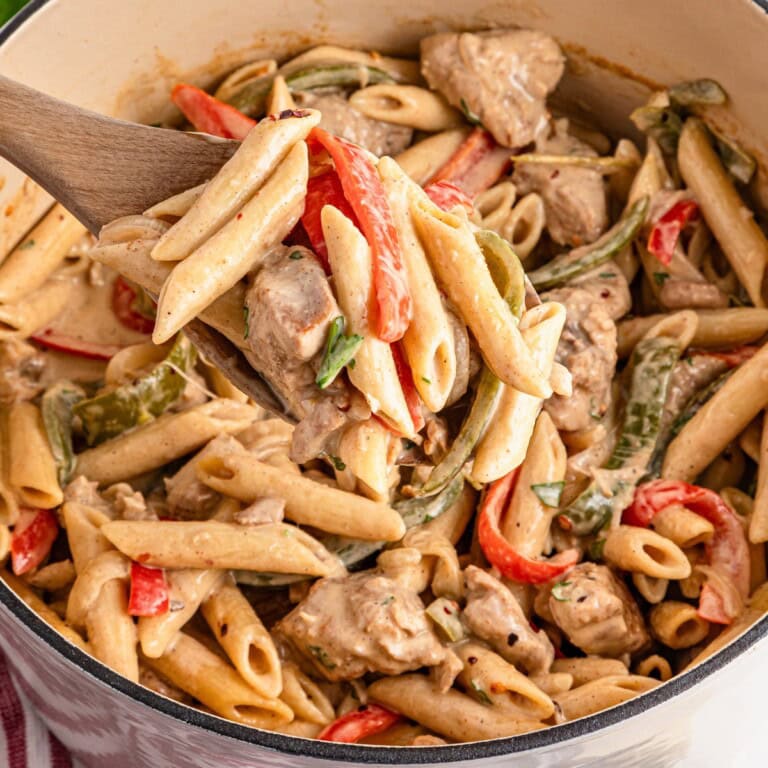 Creamy penne pasta with chicken and bell peppers in a large pot, on a wooden spoon.
