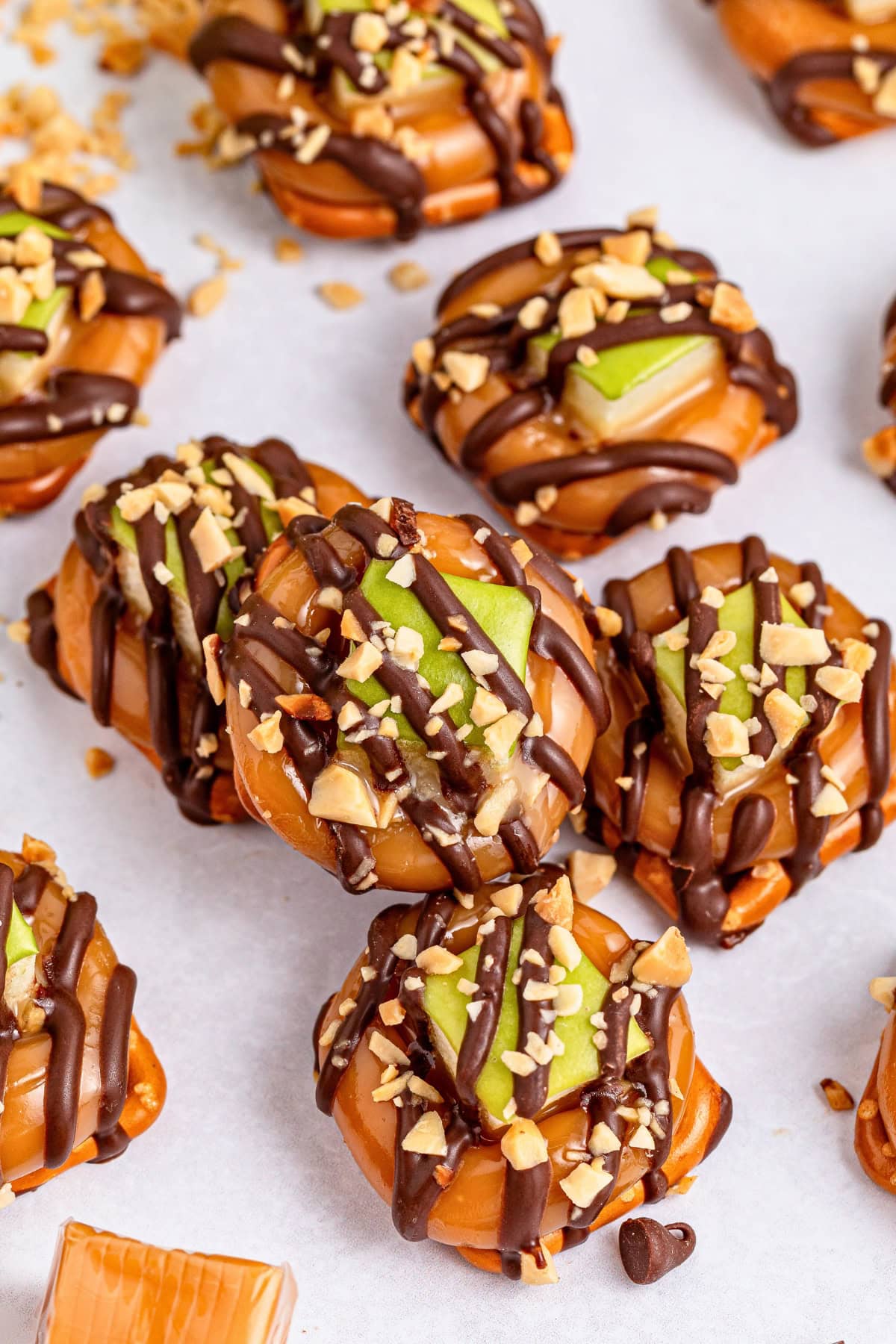 Caramel apple slices topped with chocolate drizzle and chopped nuts on parchment.