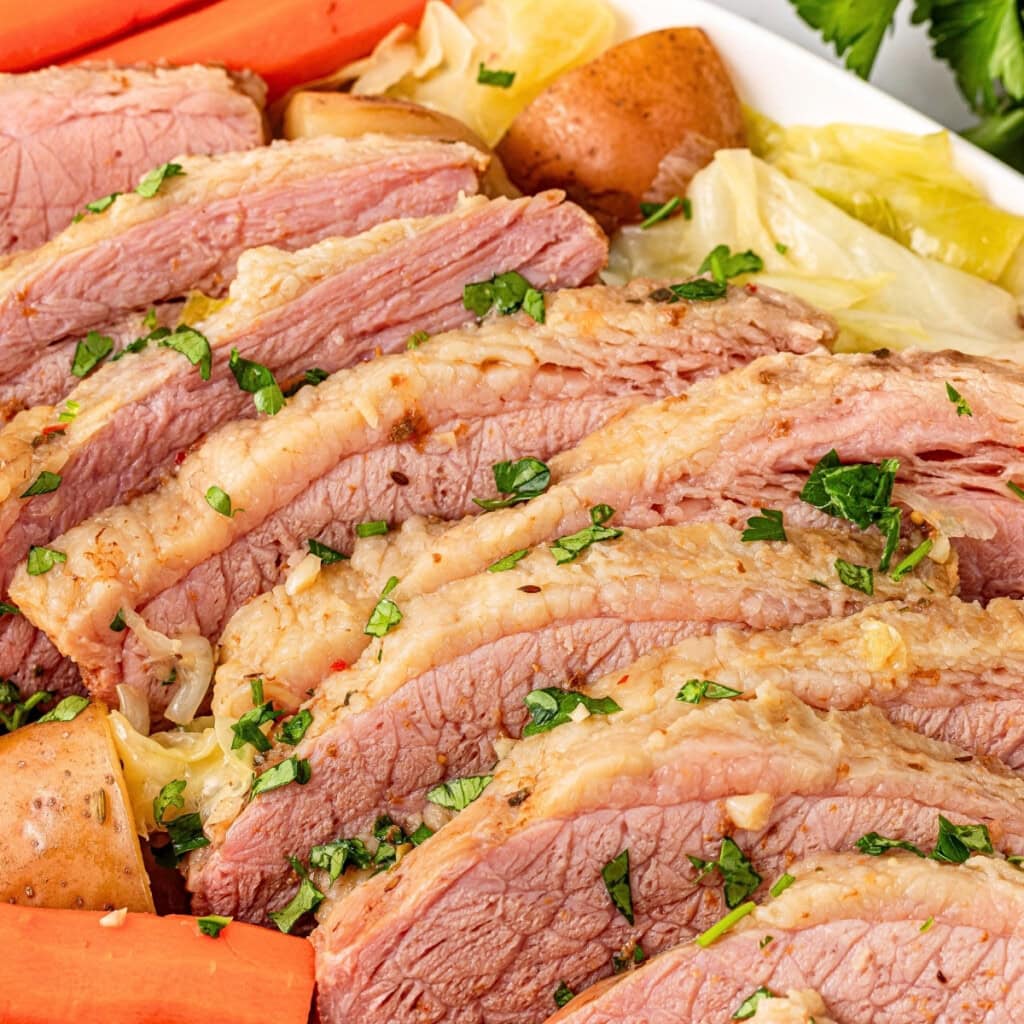 Sliced corned beef with potatoes, carrots, cabbage, and parsley garnish.