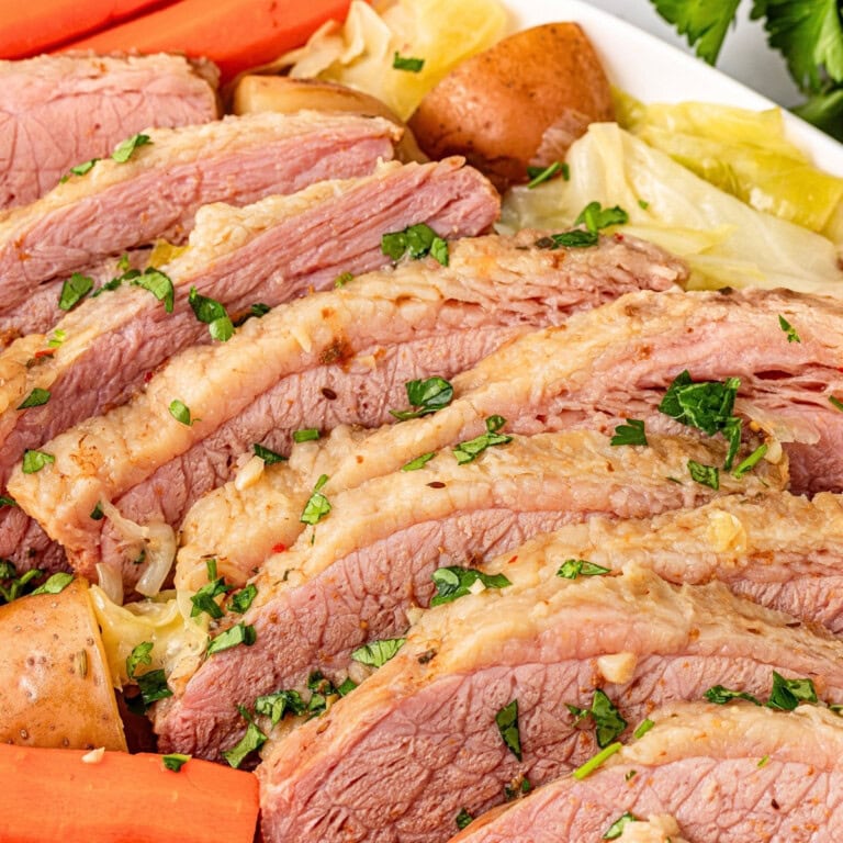 Sliced corned beef with potatoes, carrots, cabbage, and parsley garnish.