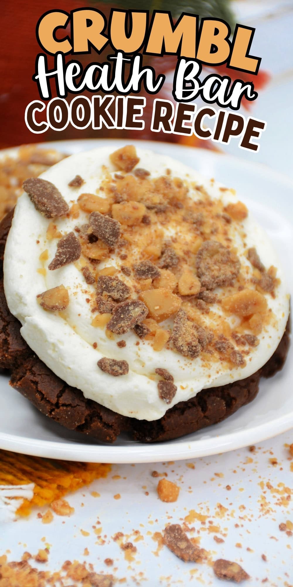 A chocolate cookie topped with cream and Heath Bar crumbles on a white plate.