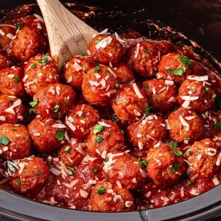 Meatballs in tomato sauce topped with parsley and cheese in a slow cooker.