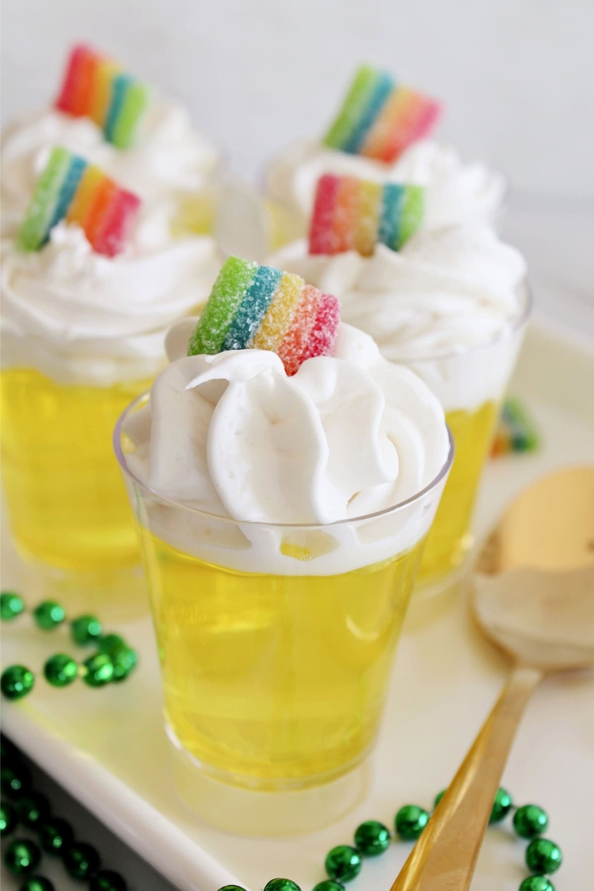Yellow gelatin cups with whipped cream and rainbow candy, garnished with beads.