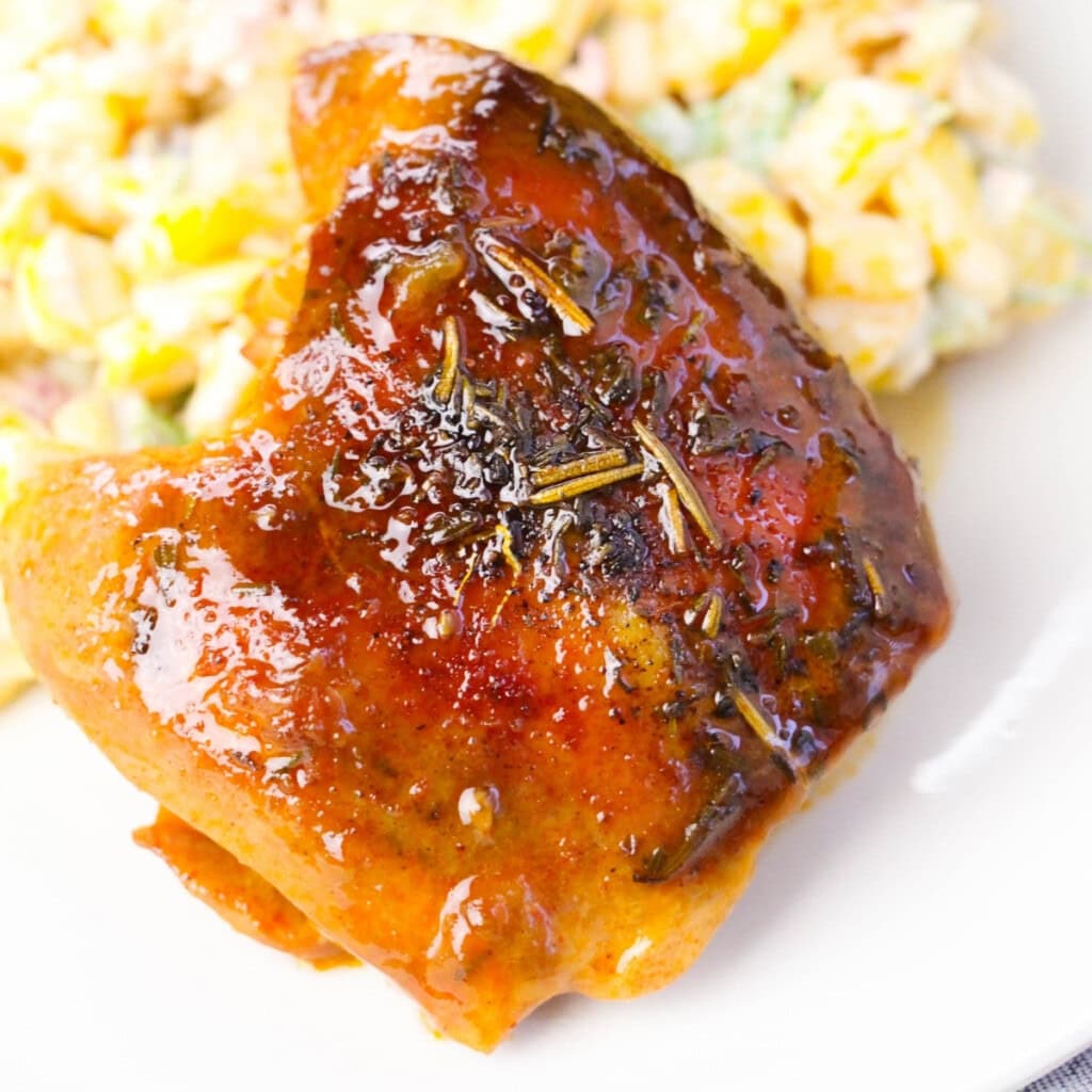 Glazed baked chicken thigh with herbs, served next to a creamy salad.