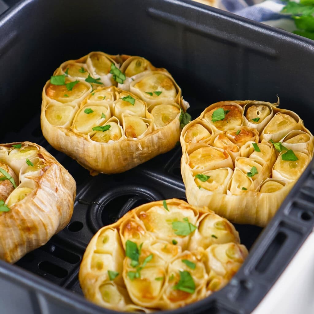 Four roasted garlic bulbs topped with parsley in an air fryer basket.