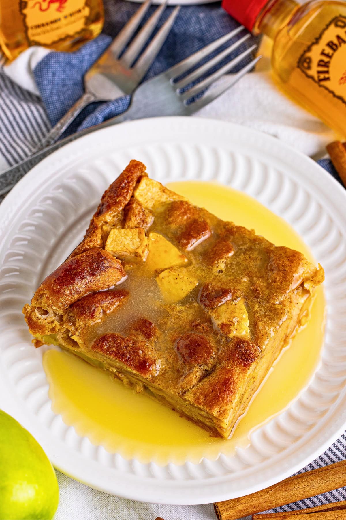A slice of bread pudding with sauce on a white plate, surrounded by ingredients.