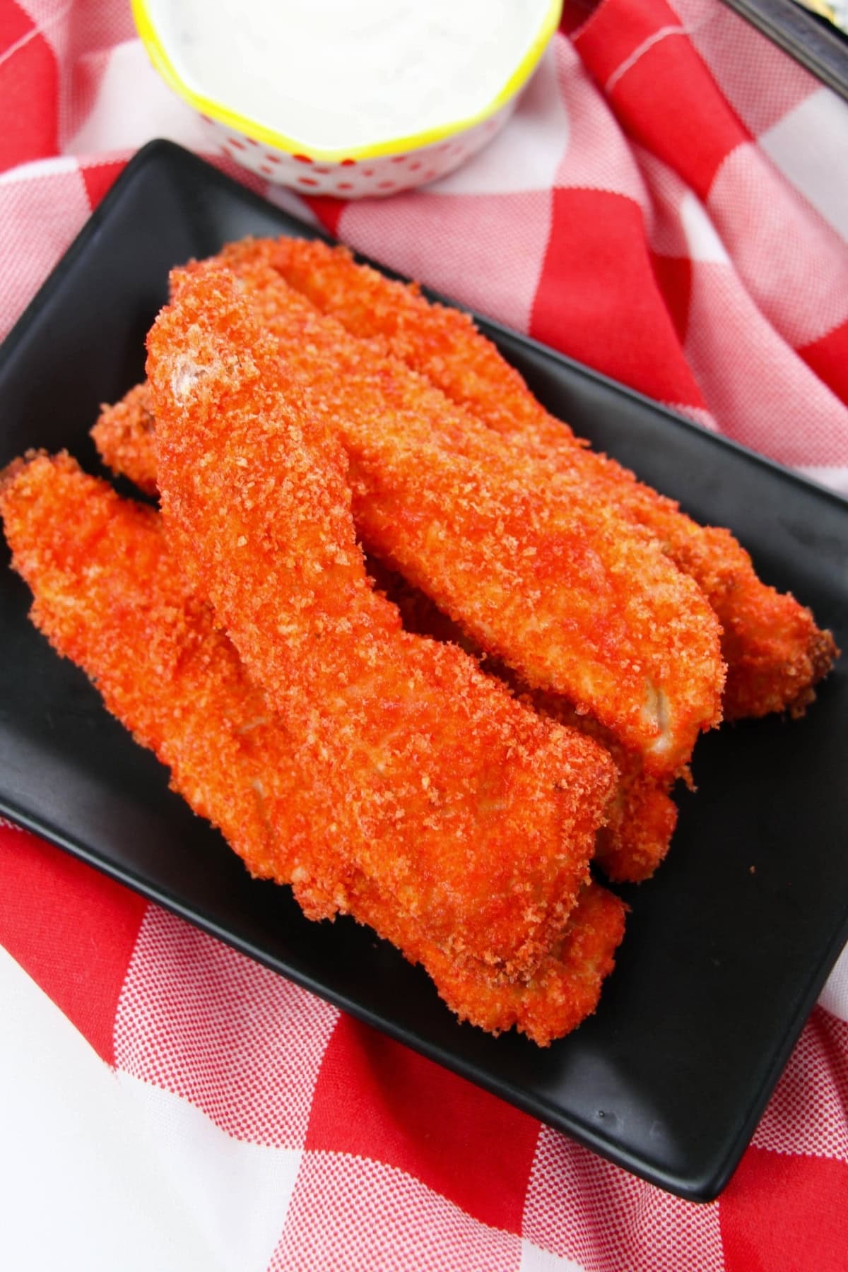 Crispy breaded chicken tenders stacked on a black plate with red checkered cloth.