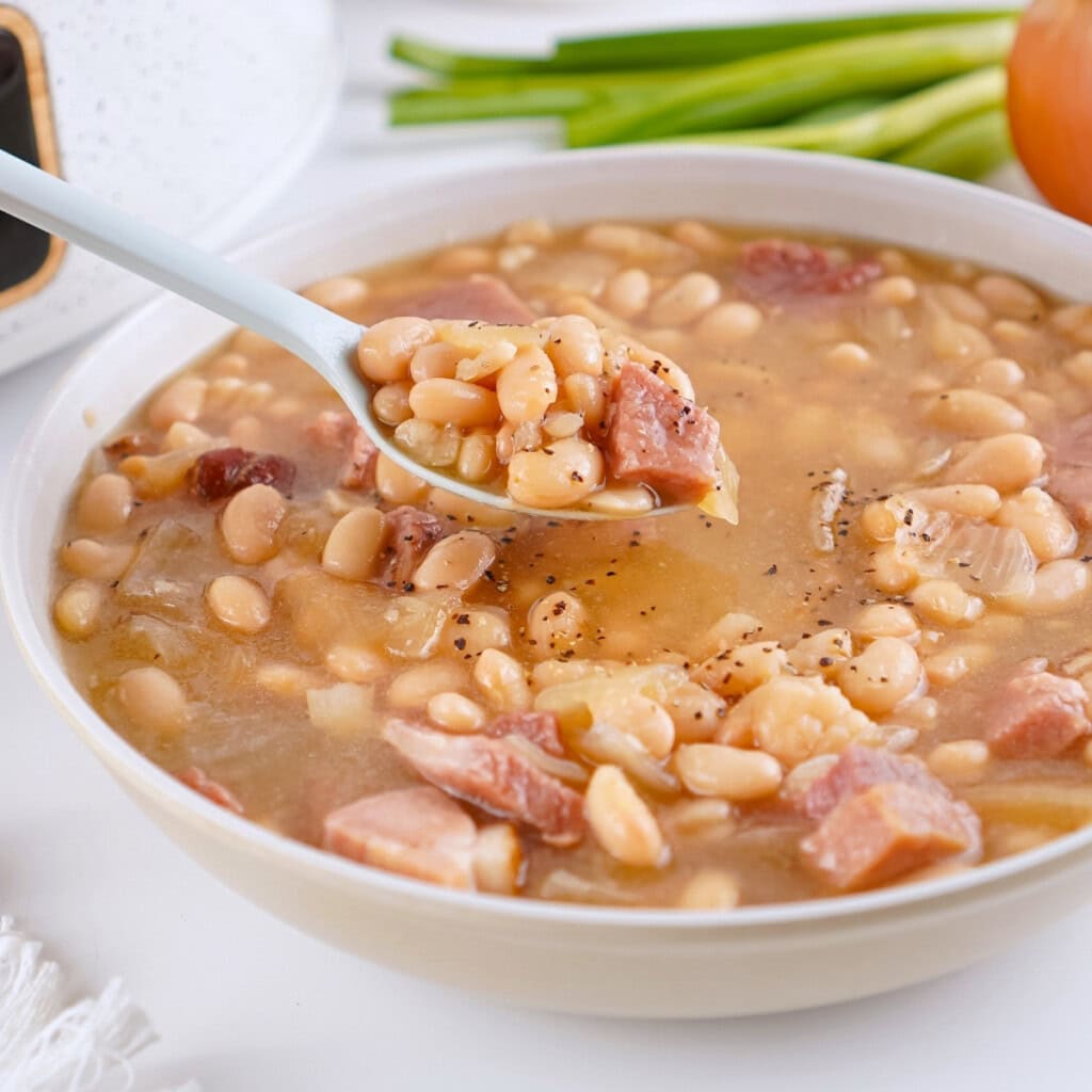 A bowl of bean and ham soup with a spoonful being lifted.