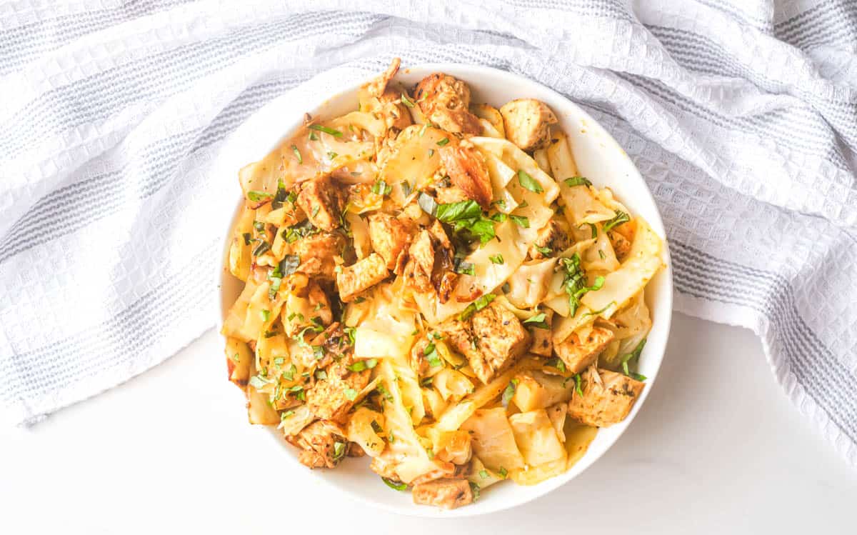 A bowl of stir-fried cabbage and tofu topped with fresh herbs, on a white cloth.