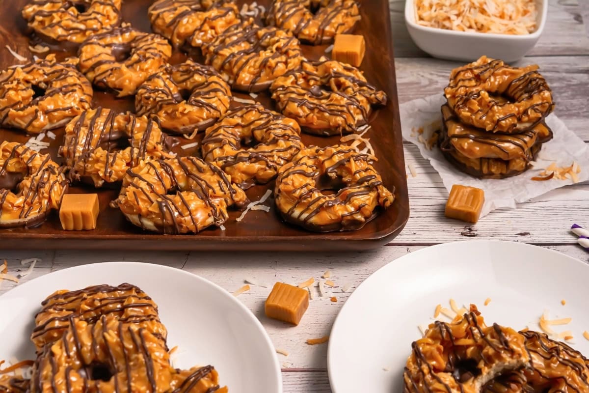 Samoa Cookies with caramel, coconut, and chocolate drizzle on plates and a baking sheet.