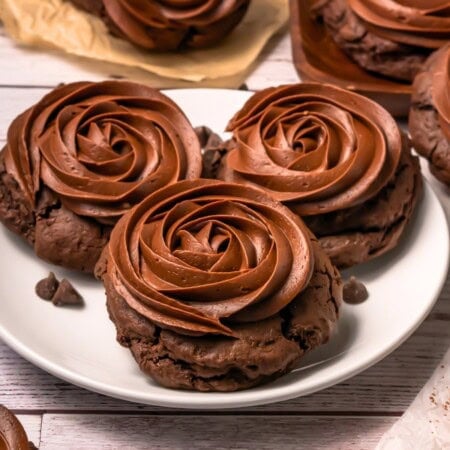 Three chocolate cookies topped with swirled chocolate frosting on a white plate.