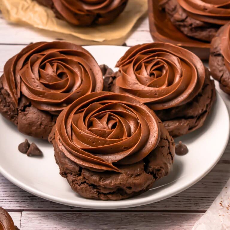 Three chocolate cookies topped with swirled chocolate frosting on a white plate.