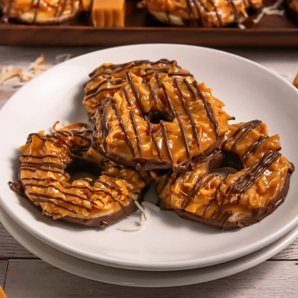 Three caramel and chocolate-drizzled cookies stacked on a white plate.