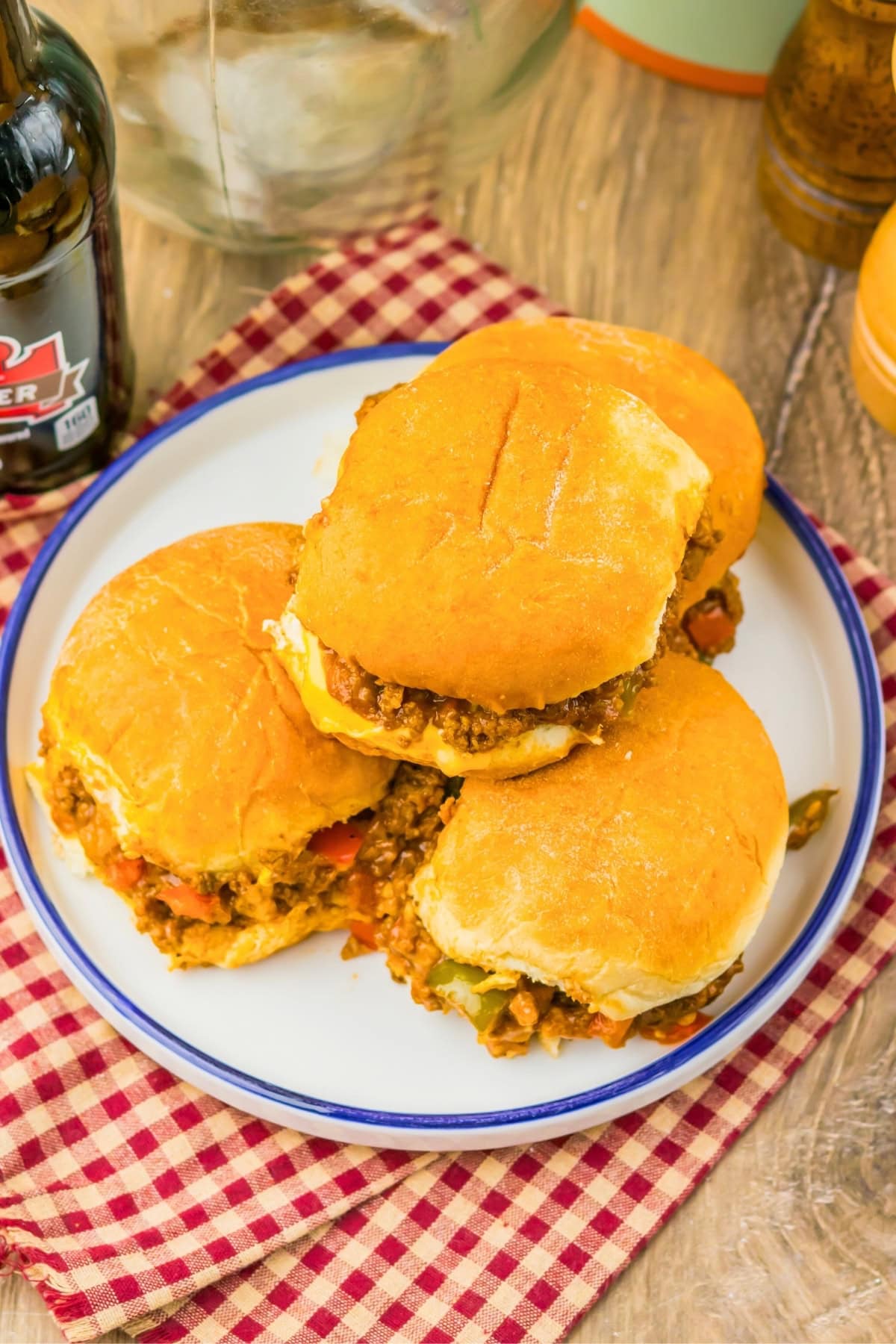 Three sloppy joe sandwiches on a white plate, set on a red checkered cloth.