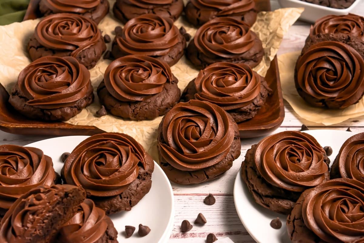 Chocolate cookies with swirled chocolate frosting on white plates and parchment paper.