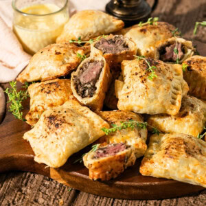 Golden puff pastry bites filled with beef and herbs on a wooden board.