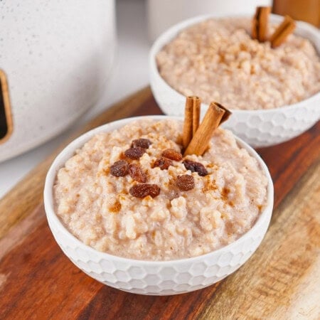 Bowl of rice pudding topped with raisins and cinnamon sticks on a wooden board.