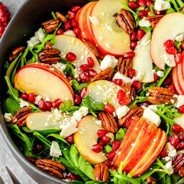Spinach salad with apple slices, pecans, pomegranate seeds, and feta cheese.