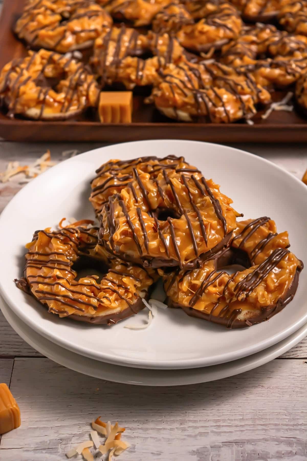 Three caramel and chocolate-drizzled cookies on a plate, more in background.