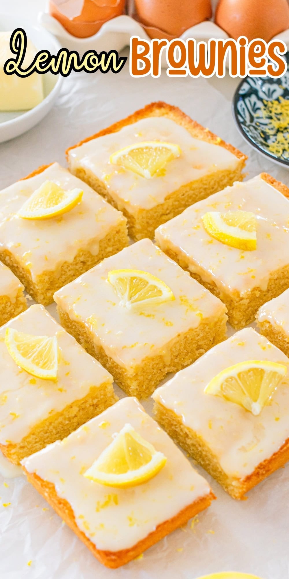 Lemon brownies topped with lemon slices, arranged on a white surface.