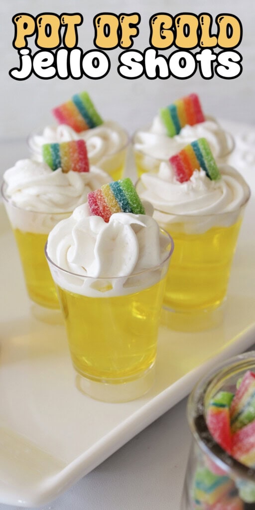 Four yellow jello shots topped with whipped cream and rainbow candy strips.
