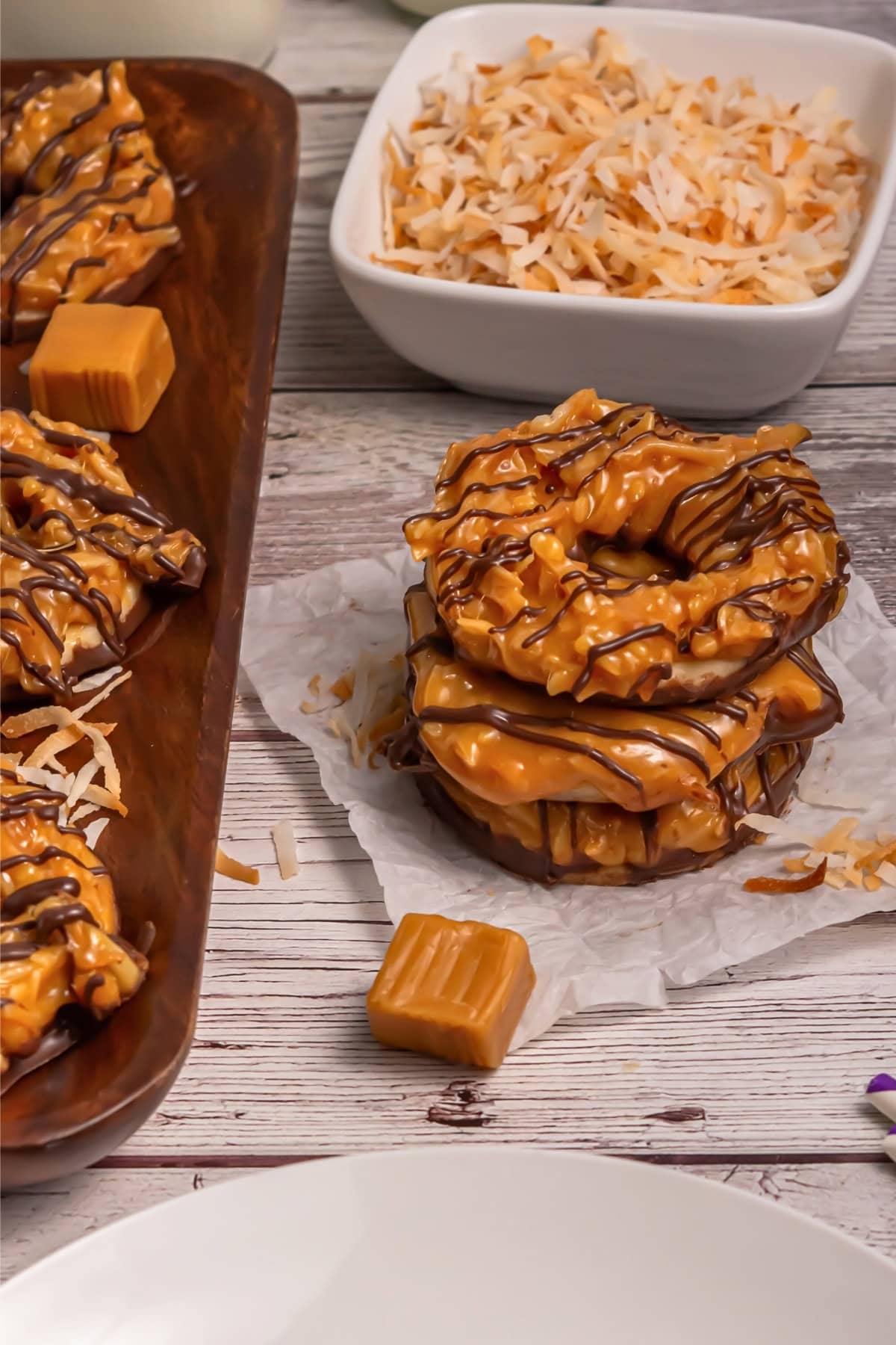 Caramel and chocolate-drizzled cookies with shredded coconut on a wooden table.